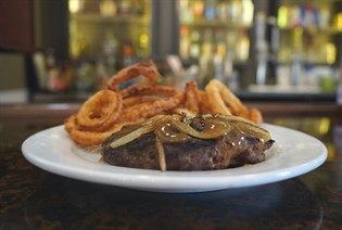 Image: A place of meat covered in glazed ionions and some fried onion rings